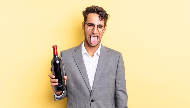 Hombre guapo hispano con actitud alegre y rebelde, bromeando y sacando la lengua. concepto de botella de vino