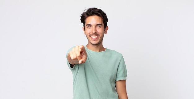 Hombre guapo hispano apuntando a la cámara con una sonrisa satisfecha, confiada y amistosa, eligiéndote