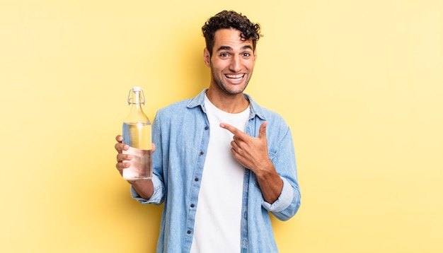 Hombre guapo hispano mirando emocionado y sorprendido apuntando hacia un lado. concepto de botella de agua