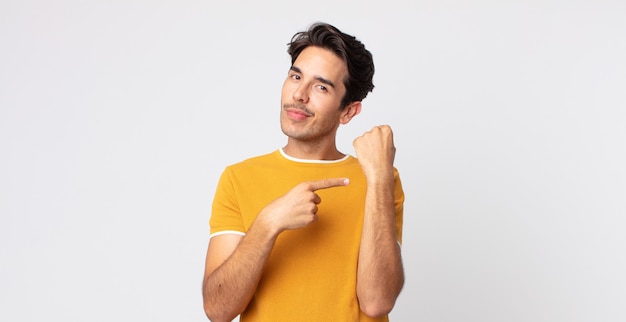 Hombre guapo hispano que parece impaciente y enojado, apuntando al reloj, pidiendo puntualidad, quiere llegar a tiempo