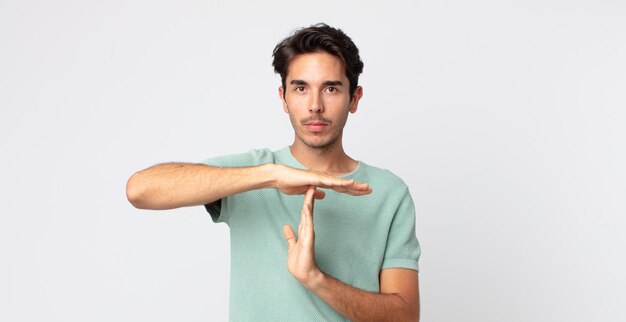 Hombre guapo hispano que parece serio, severo, enojado y disgustado, haciendo el signo de tiempo de espera