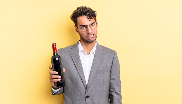 Hombre guapo hispano que se siente desconcertado y confundido. concepto de botella de vino