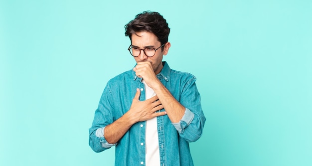 Hombre guapo hispano que se siente enfermo con dolor de garganta y síntomas de gripe tosiendo con la boca cubierta