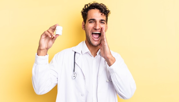 Hombre guapo hispano que se siente feliz, dando un gran grito con las manos al lado de la boca. concepto de píldoras de botella de médico