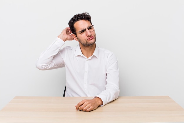 Hombre guapo hispano que se siente perplejo y confundido rascándose la cabeza del hombre de negocios y el concepto de escritorio