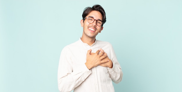 Hombre guapo hispano que se siente romántico, feliz y enamorado, sonriendo alegremente y tomados de la mano cerca del corazón