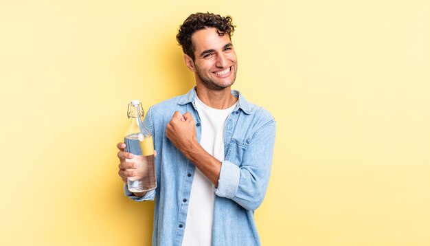 Hombre guapo hispano sintiéndose feliz y enfrentando un desafío o celebrando. concepto de botella de agua