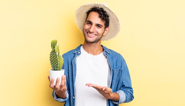 Hombre guapo hispano sonriendo alegremente, sintiéndose feliz y mostrando un concepto de agricultor y cactus