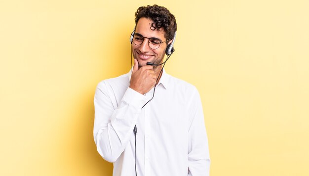 Hombre guapo hispano sonriendo con una expresión feliz y segura con la mano en la barbilla. concepto de telemarketer