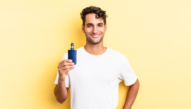 Hombre guapo hispano sonriendo felizmente con una mano en la cadera y confiado. concepto de vaporizador