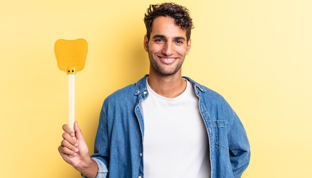 Hombre guapo hispano sonriendo felizmente con una mano en la cadera y confiado. mata moscas concepto