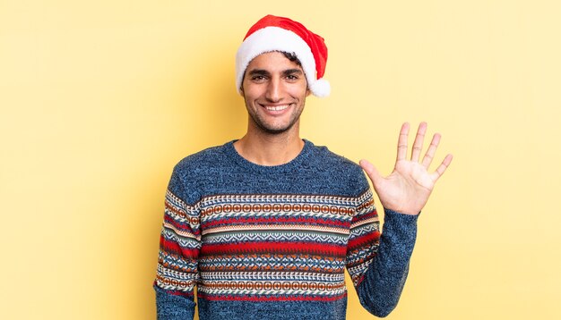 Hombre guapo hispano sonriendo y mirando amistoso, mostrando el número cinco. concepto de navidad