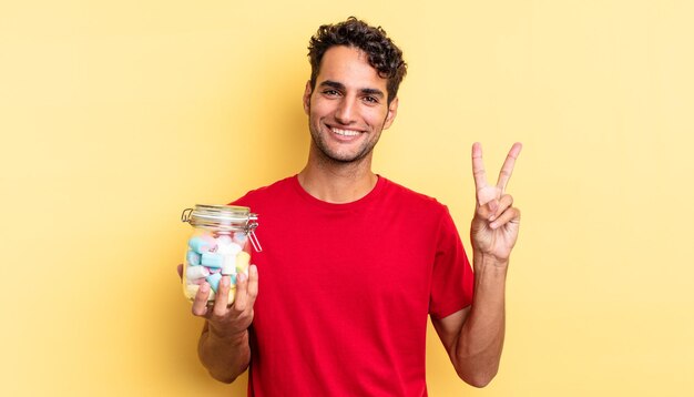 Hombre guapo hispano sonriendo y mirando amistoso, mostrando el número dos. concepto de caramelos