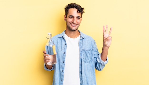 Hombre guapo hispano sonriendo y mirando amistoso, mostrando el número tres. concepto de botella de agua