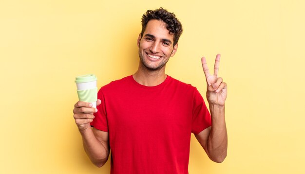 Hombre guapo hispano sonriendo y mirando feliz, gesticulando victoria o paz. concepto de café para llevar