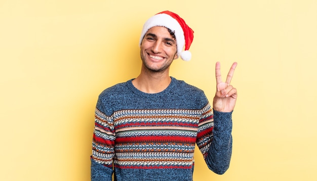 Hombre guapo hispano sonriendo y mirando feliz, gesticulando victoria o paz. concepto de navidad