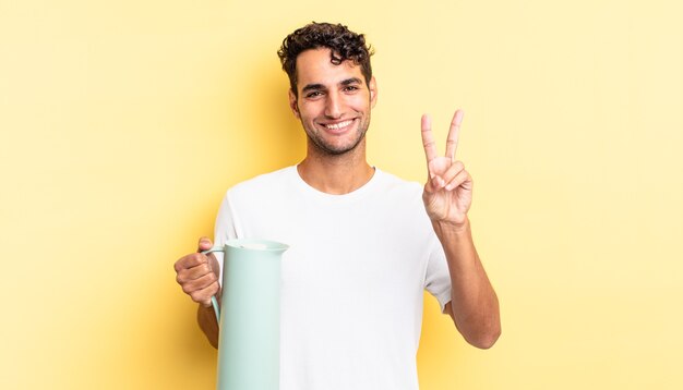 Hombre guapo hispano sonriendo y mirando feliz, gesticulando victoria o paz. concepto de termo de café