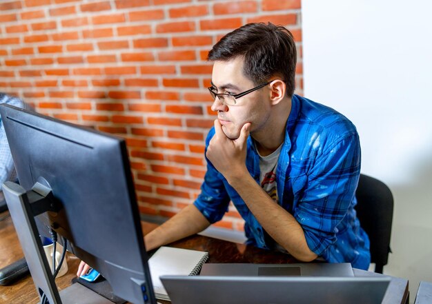 Hombre guapo inteligente que trabaja con internet en la computadora portátil. Hombre con estilo moderno sentado en la mesa.