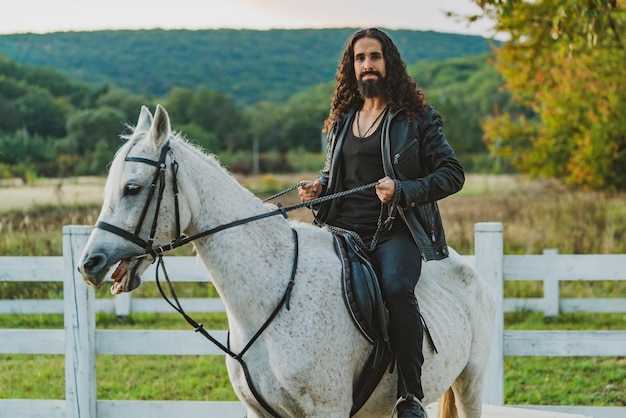 Hombre guapo jinete a caballo Ecuestre monta su caballo blanco bien parecido Hombre guapo montando a caballo en la granja Atractivo hombre sentado en un semental blanco en el rancho en otoño