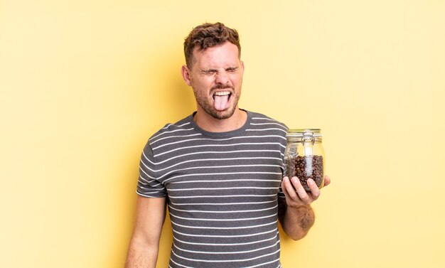 Hombre guapo joven con actitud alegre y rebelde, bromeando y sacando la lengua concepto de granos de café