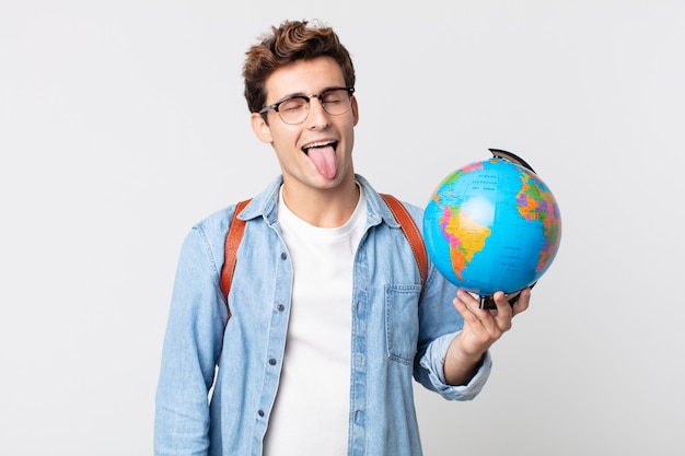 Hombre guapo joven con actitud alegre y rebelde, bromeando y sacando la lengua. estudiante sosteniendo un mapa del globo terráqueo