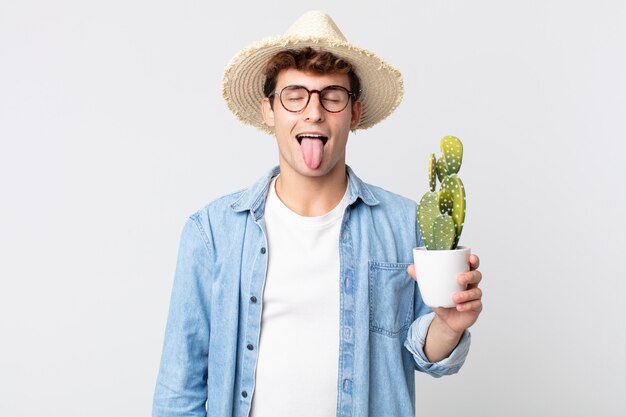 Hombre guapo joven con actitud alegre y rebelde, bromeando y sacando la lengua. granjero sosteniendo un cactus decorativo