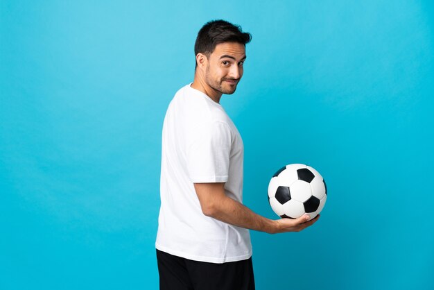 Hombre guapo joven aislado en azul con balón de fútbol