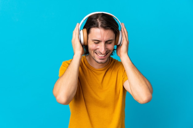 Hombre guapo joven aislado en azul escuchando música