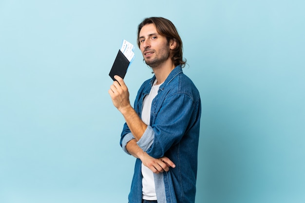 Hombre guapo joven aislado en azul feliz de vacaciones con pasaporte y billetes de avión