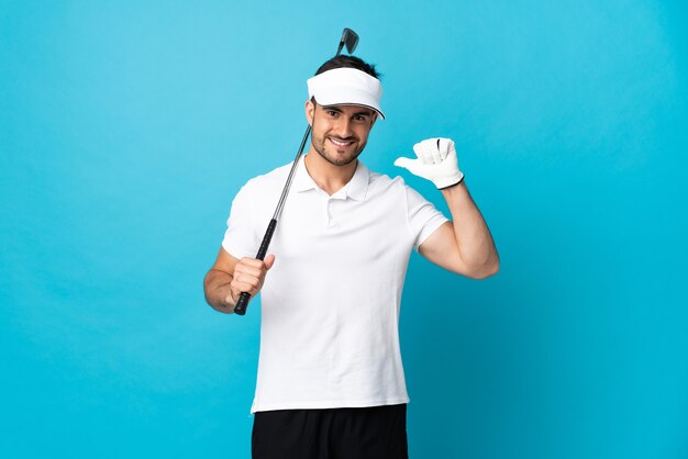 Hombre guapo joven aislado en azul jugando al golf y orgulloso de sí mismo