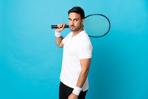 Hombre guapo joven aislado en azul jugando al tenis