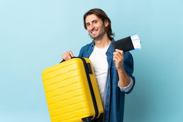 Hombre guapo joven aislado en azul en vacaciones con maleta y pasaporte