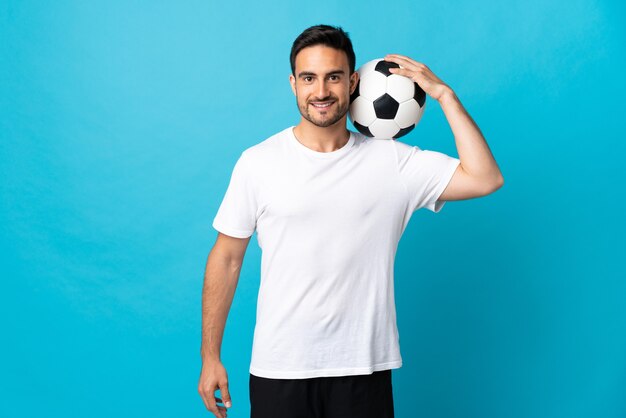 Hombre guapo joven aislado en la pared azul con balón de fútbol