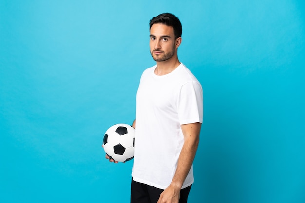 Hombre guapo joven aislado sobre fondo azul con balón de fútbol