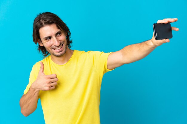 Hombre guapo joven aislado sobre fondo azul haciendo un selfie con teléfono móvil