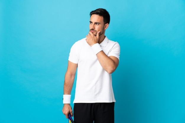 Hombre guapo joven aislado sobre fondo azul jugando al tenis y pensando