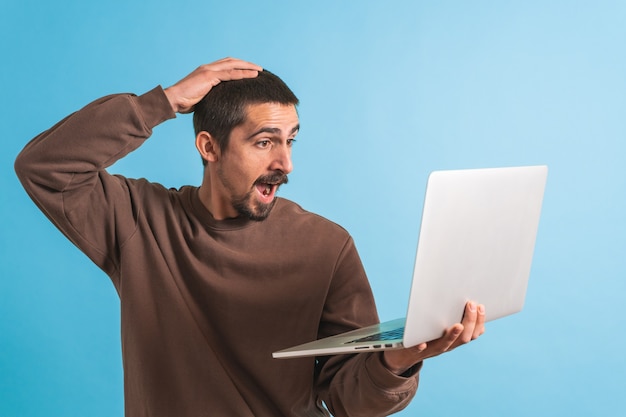 Hombre guapo joven aislado sobre fondo azul usando su computadora portátil trabajando Copiar texto de espacio