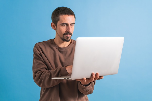 Hombre guapo joven aislado sobre fondo azul usando su computadora portátil trabajando Copiar texto de espacio