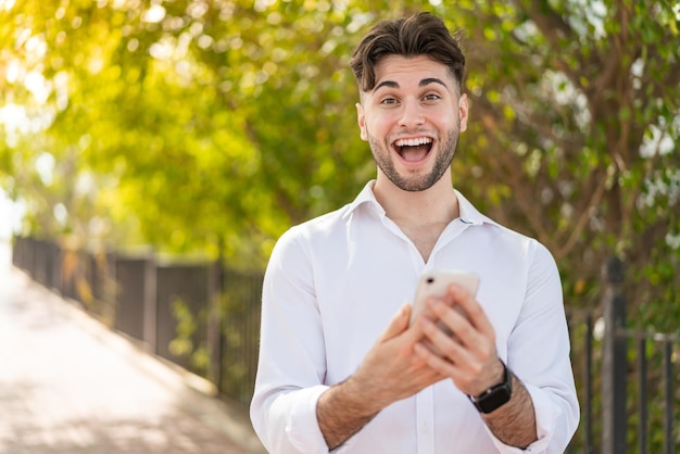 Foto hombre guapo joven al aire libre sorprendido y enviando un mensaje