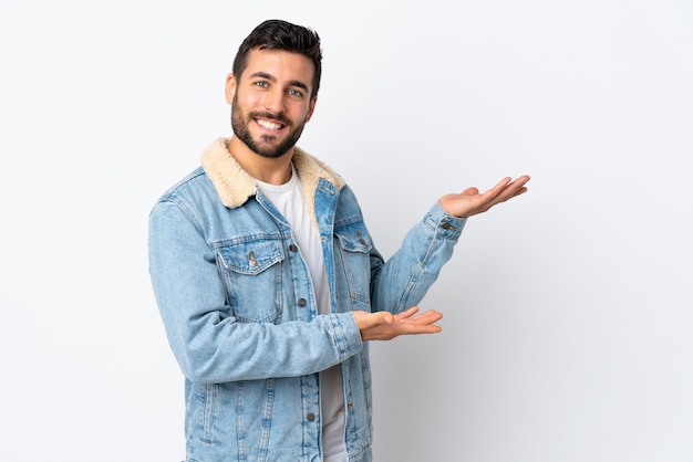 Hombre guapo joven con barba aislado en blanco extendiendo las manos hacia el lado para invitar a venir