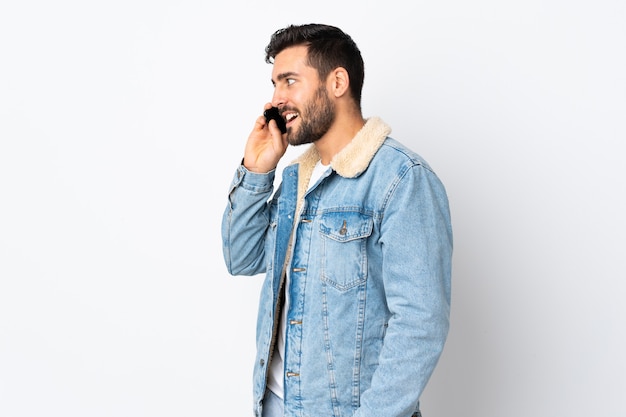 Hombre guapo joven con barba aislado en blanco manteniendo una conversación con el teléfono móvil con alguien
