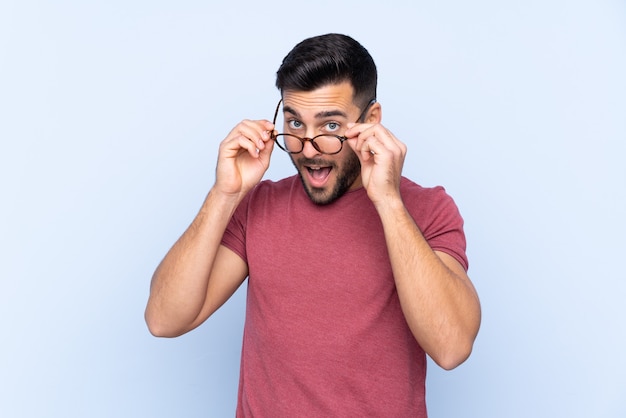 Hombre guapo joven con barba aislado con gafas y sorprendido