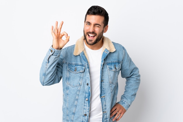 Hombre guapo joven con barba aislado en la pared blanca que muestra signo bien con los dedos