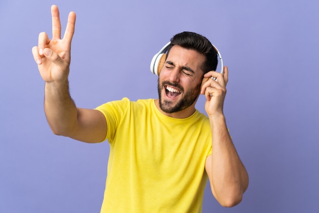 Hombre guapo joven con barba aislado en la pared púrpura escuchando música y cantando