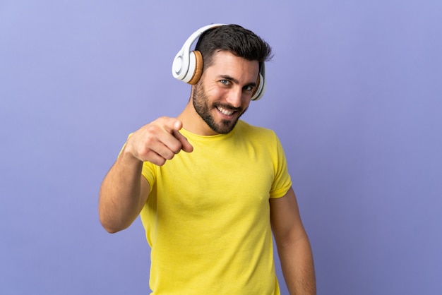 Hombre guapo joven con barba aislado en la pared púrpura escuchando música