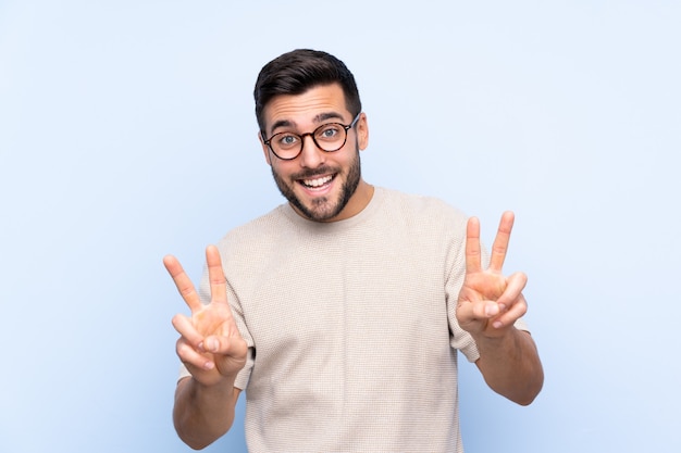 Hombre guapo joven con barba azul aislado sonriendo mostrando el signo de la victoria