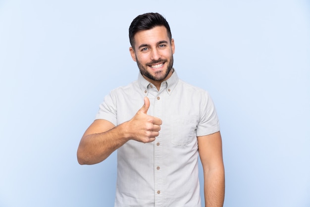 Hombre guapo joven con barba sobre fondo azul aislado dando un pulgar hacia arriba gesto