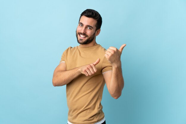 Hombre guapo joven con barba sobre pared aislada apuntando hacia el lado para presentar un producto