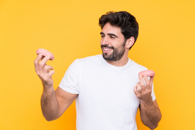 Hombre guapo joven con barba sobre pared amarilla aislada con donas con expresión feliz