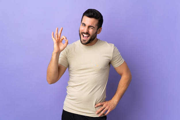 Hombre guapo joven con barba sobre la pared que muestra signo bien con los dedos